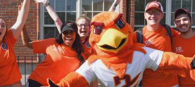 Benny Hawk mascot and students clad in orange cheer and smile for the camera.